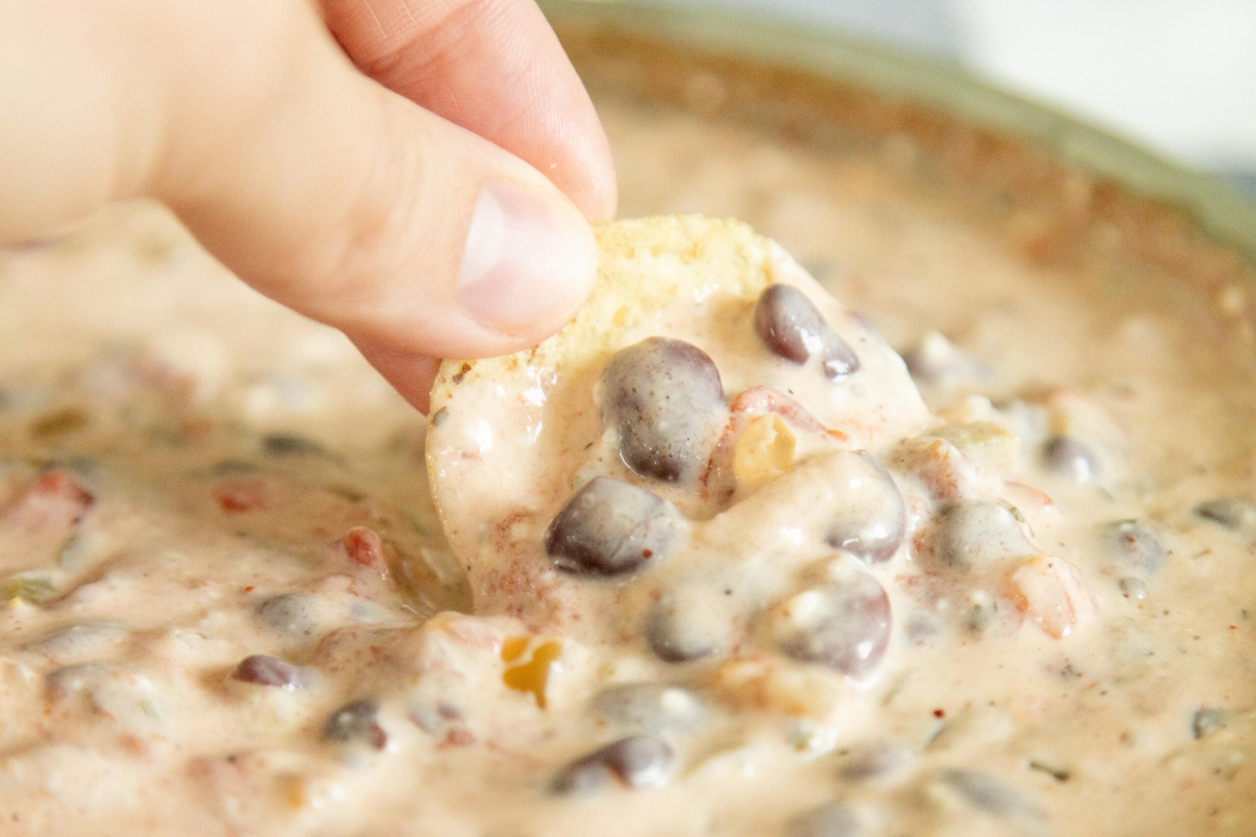 hand holding a tortilla chip taking a scoop of creamy salsa bean dip