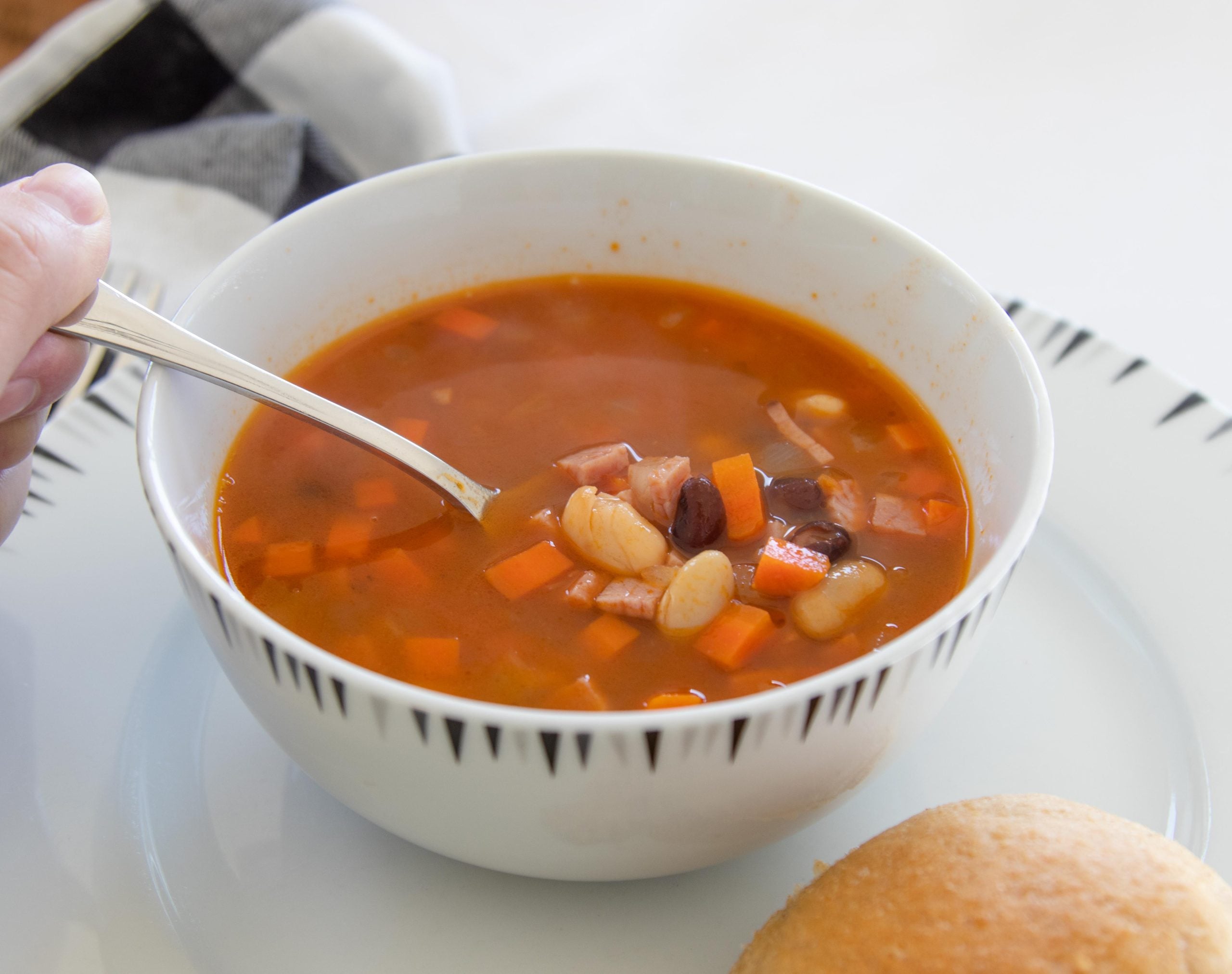 bowl of ham and bean soup on a white flat plate