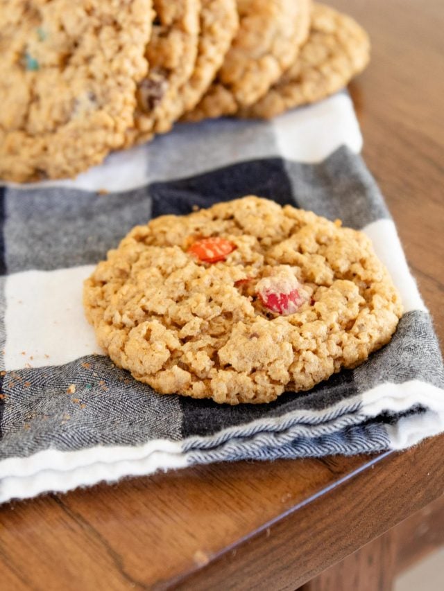 a row of monster cookies setting on a balck and white checked kitchen towel