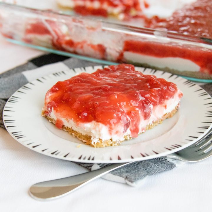 serving of strawberry delight dessert on a plate with the pan of dessert nearby