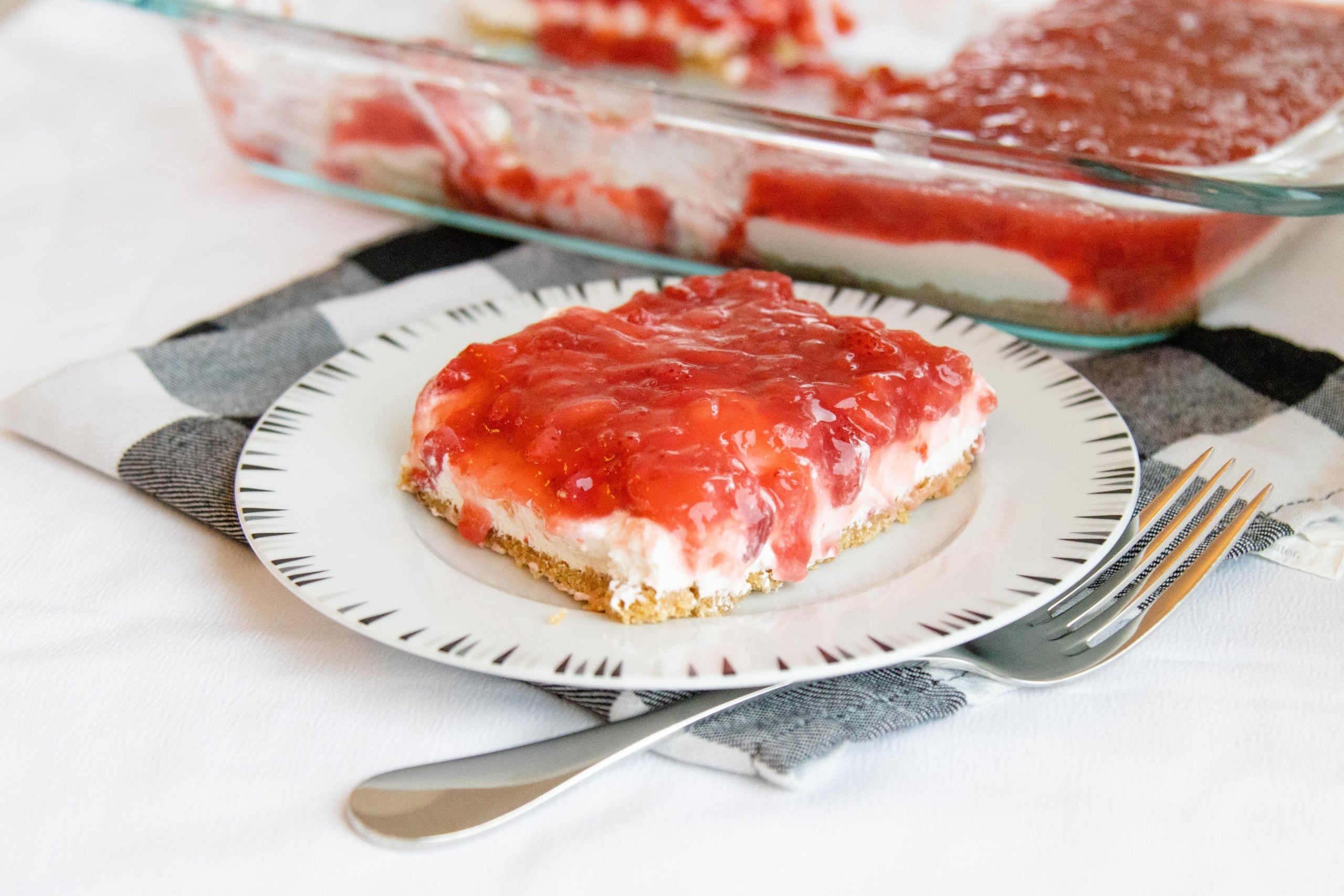 serving of strawberry delight dessert on a plate with the pan of dessert nearby