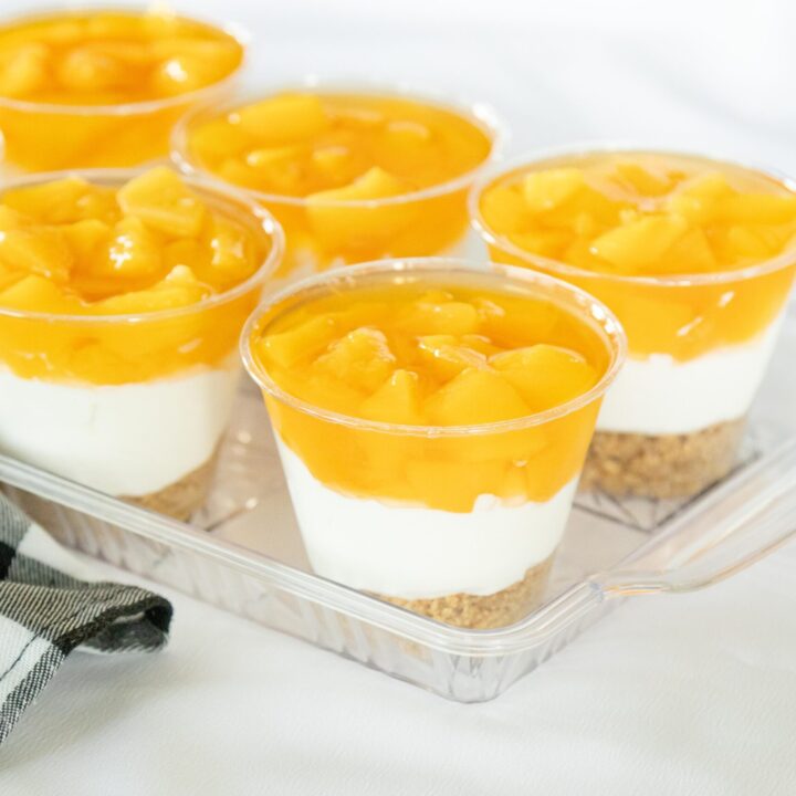 finished peaches and cream dessert cups on a clear tray on a white table