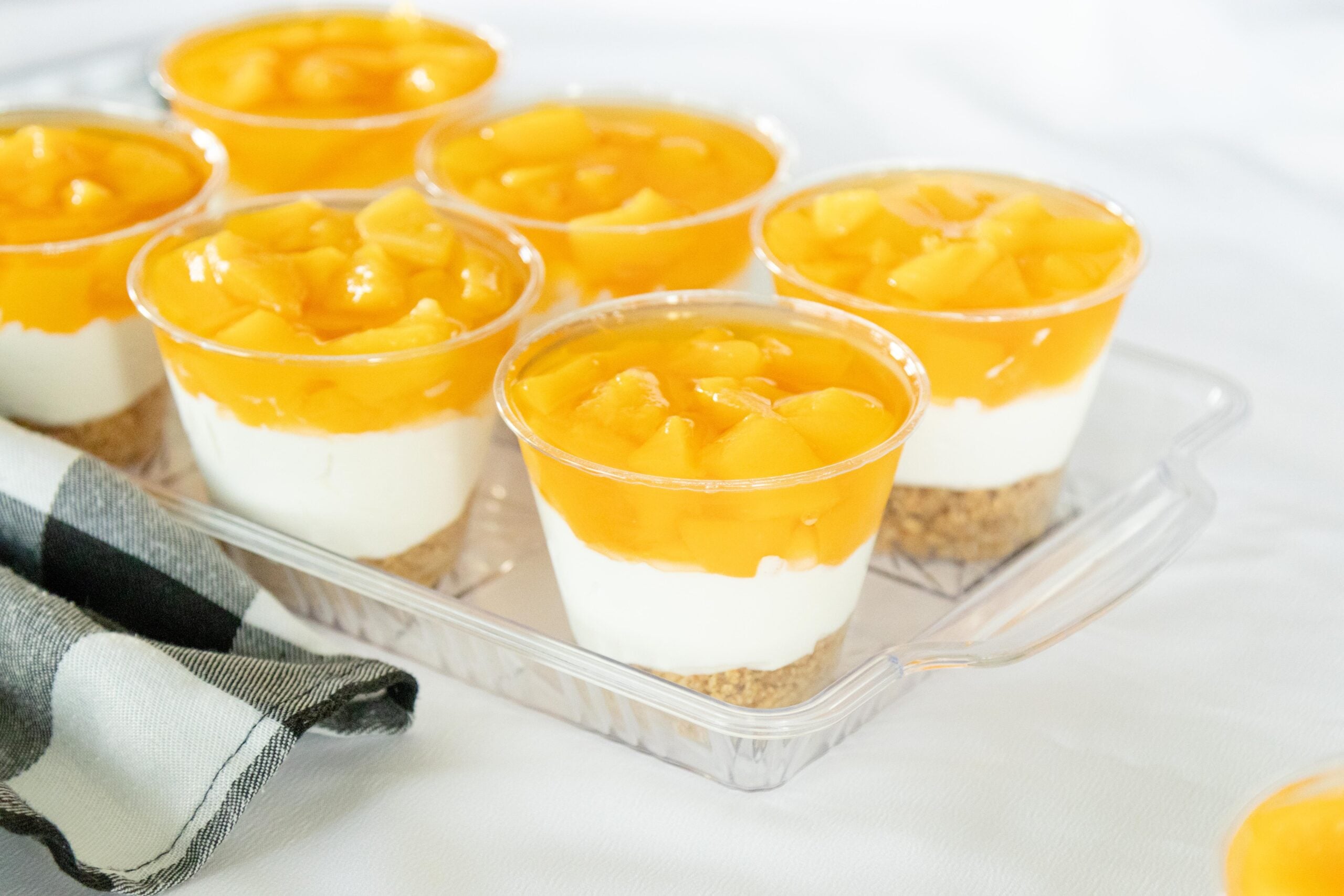 finished peaches and cream dessert cups on a clear tray on a white table