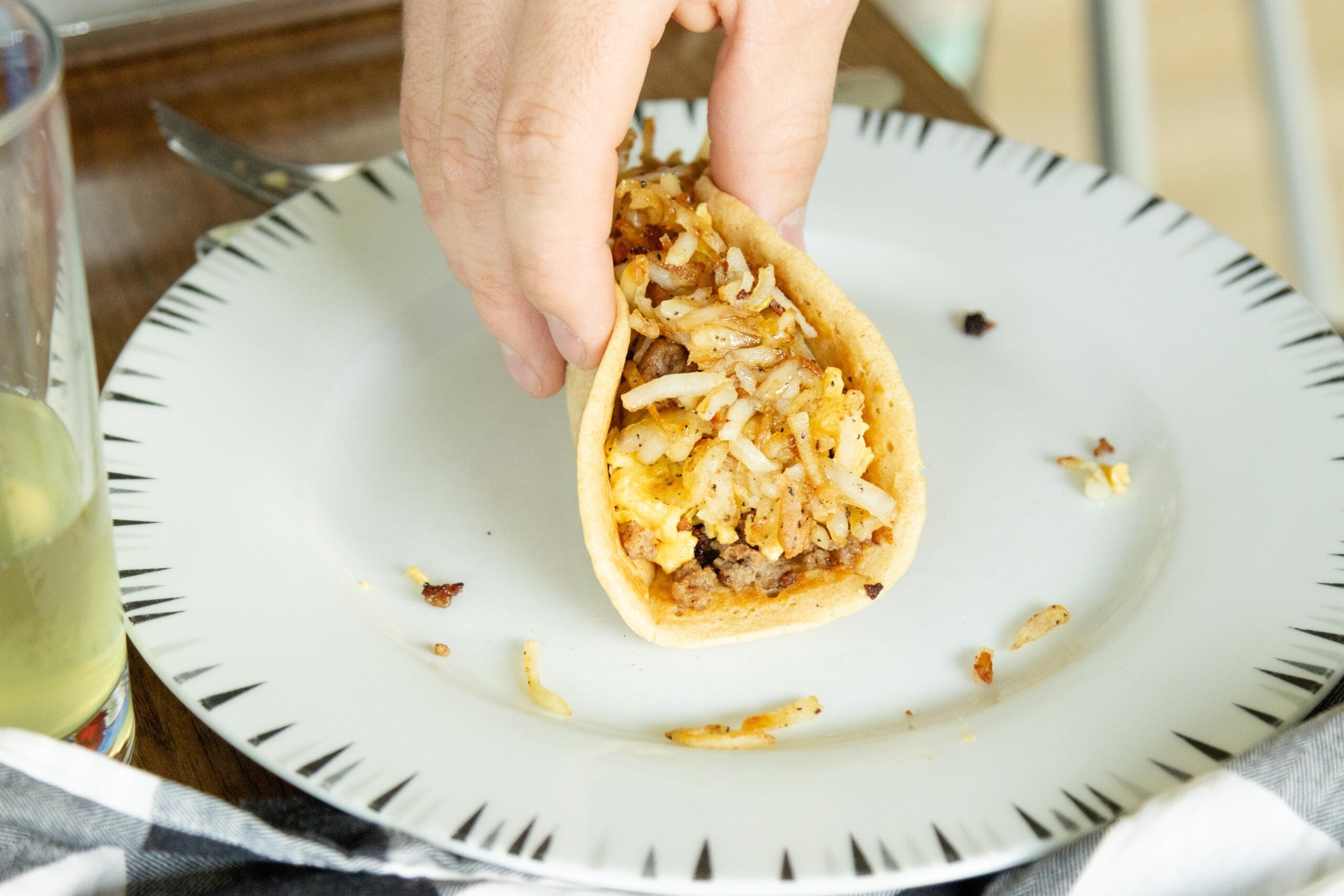 hand holding a pancake breakfast taco on a white plate