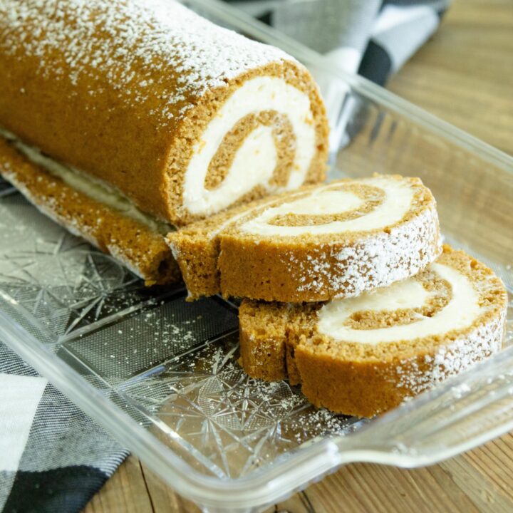 pumpkin cake roll on a clear tray with two slices laying in front of it
