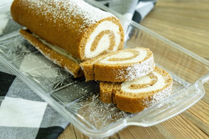 pumpkin cake roll on a clear tray with two slices laying in front of it