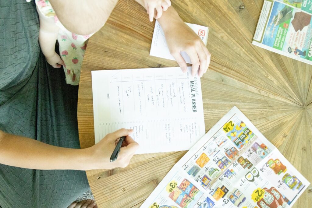 hand writing on the reverse meal plan with a baby standing nearby