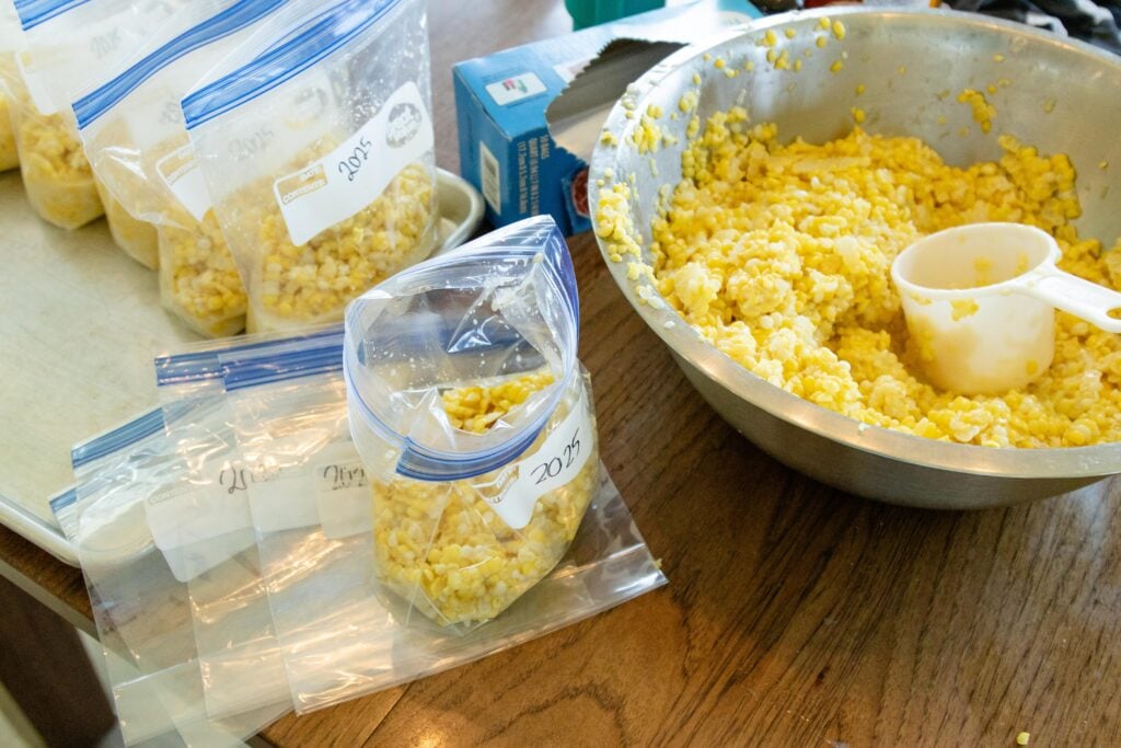 a dish of cut corn on the table with a few filled bags of corn setting beside