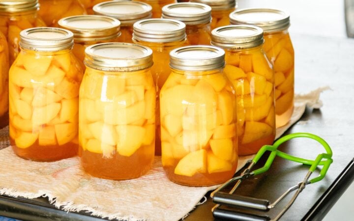 canned peaches setting on a cloth on the table with the jar lifter laying nearby