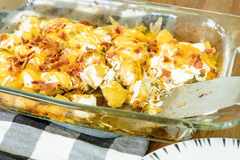 a pan of loaded chicken and vegetables on the table with a serving taken out of it