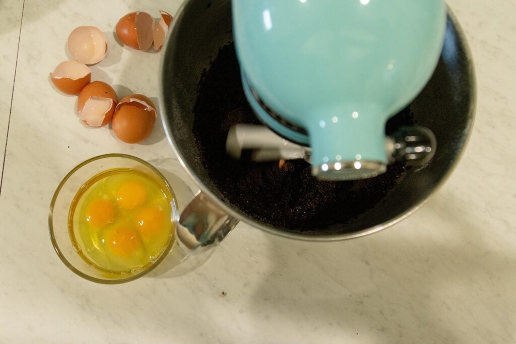 chocolate mixture in the stand mixer with the eggs setting nearby