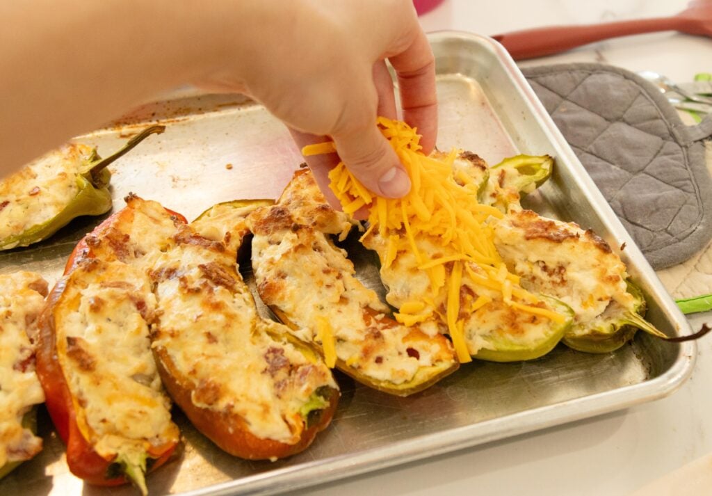 hand spreading cheese on the stuffed peppers