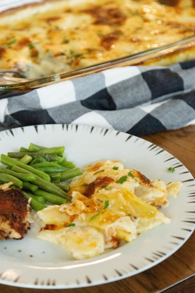 a serving of scalloped potatoes on a plate with beans and turkey croquettes