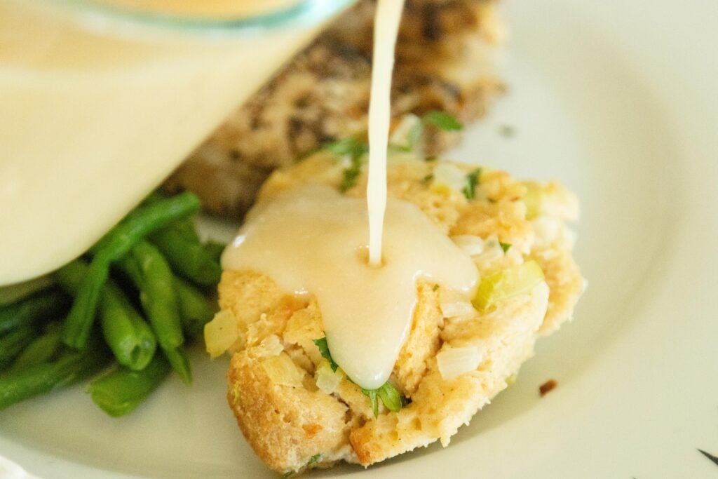 drizzling gravy over a serving of bread stuffing on a plate