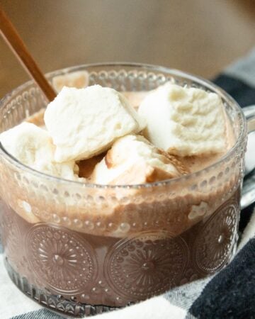 a clear glass mug of hot chocolate with some homemade marshmallows on the top