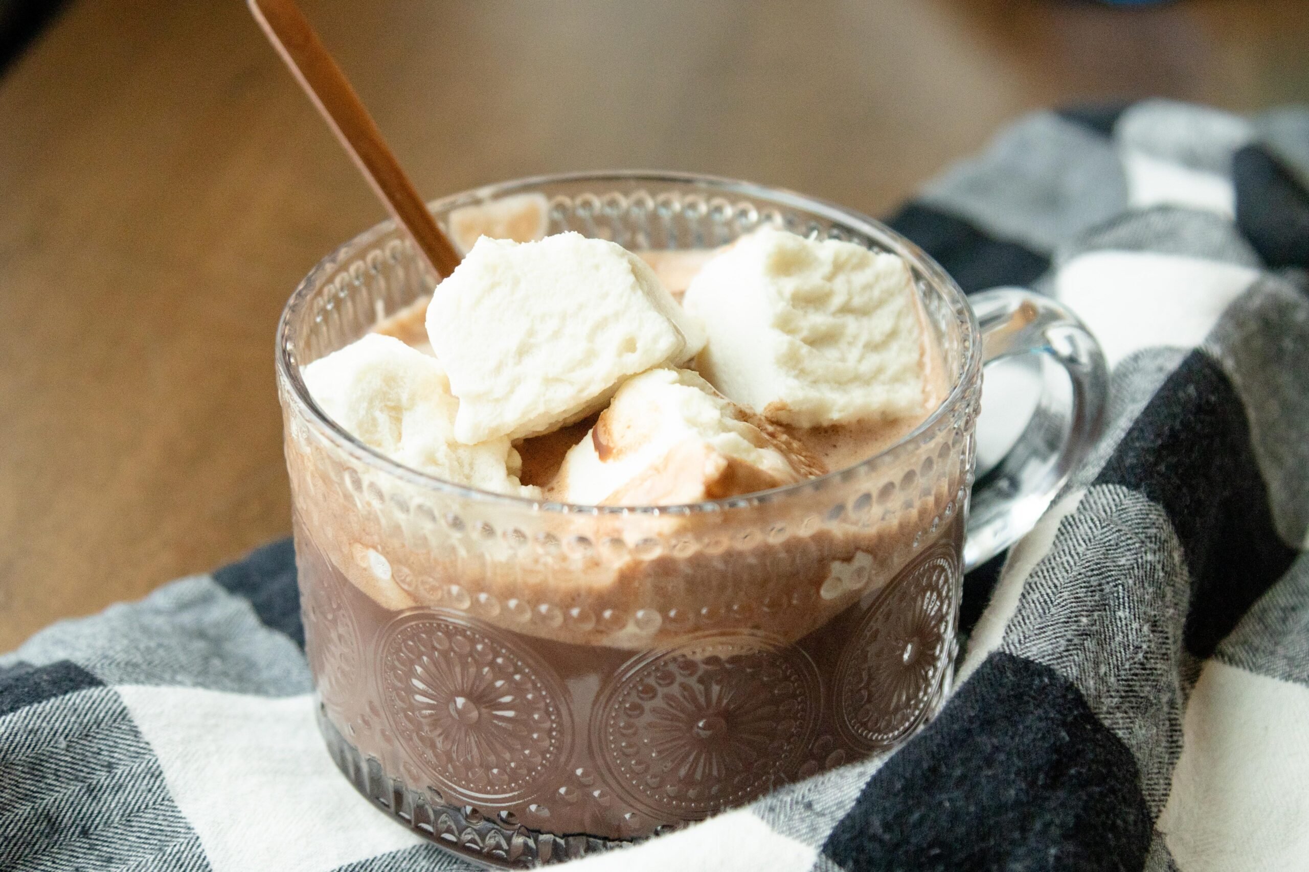 a clear glass mug of hot chocolate with some homemade marshmallows on the top