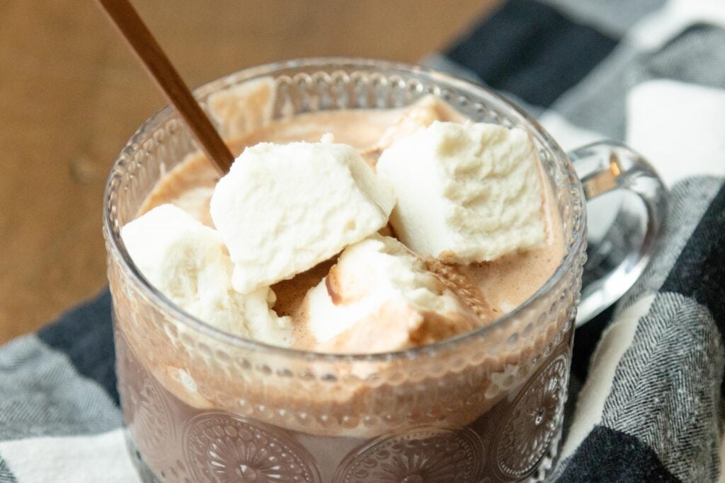 a clear glass mug of hot chocolate with some homemade marshmallows on the top