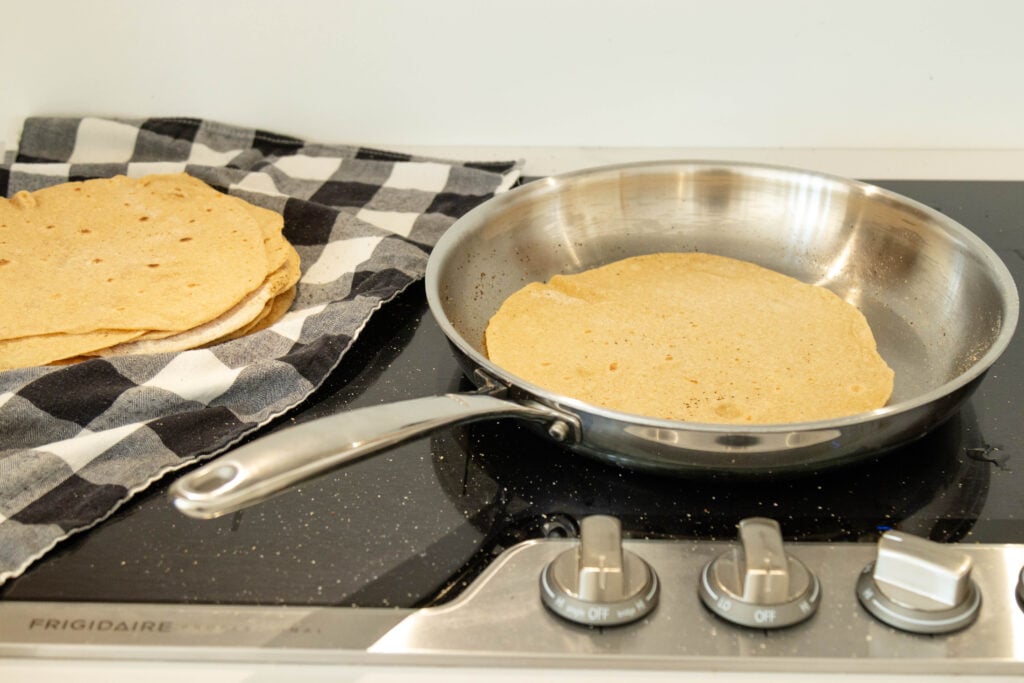 frying pan on the stovetop with a tortilla inside and a stack of tortillas beside it