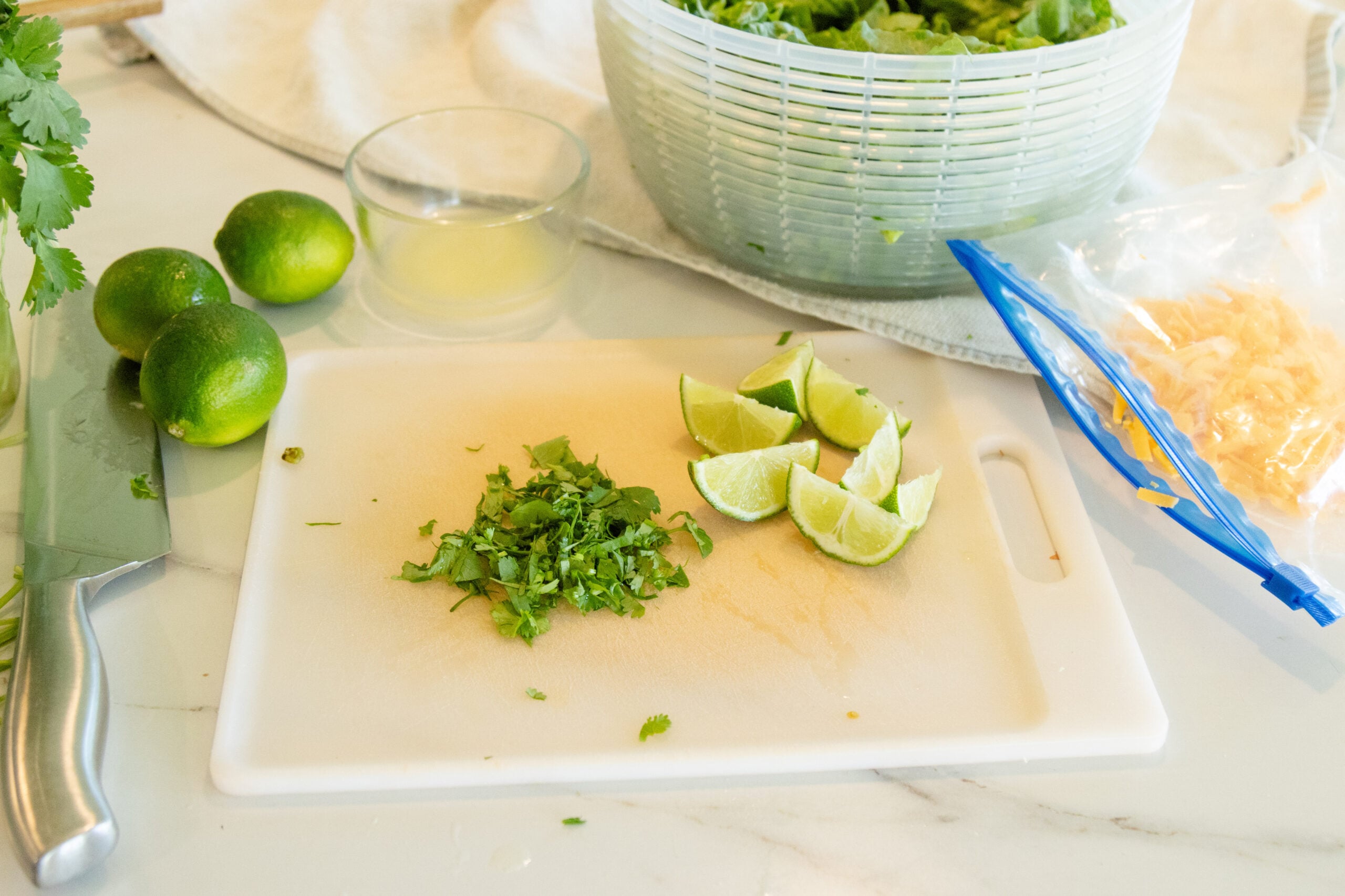 cutting board with cilantro and lime wedges on it with other ingredients nearby