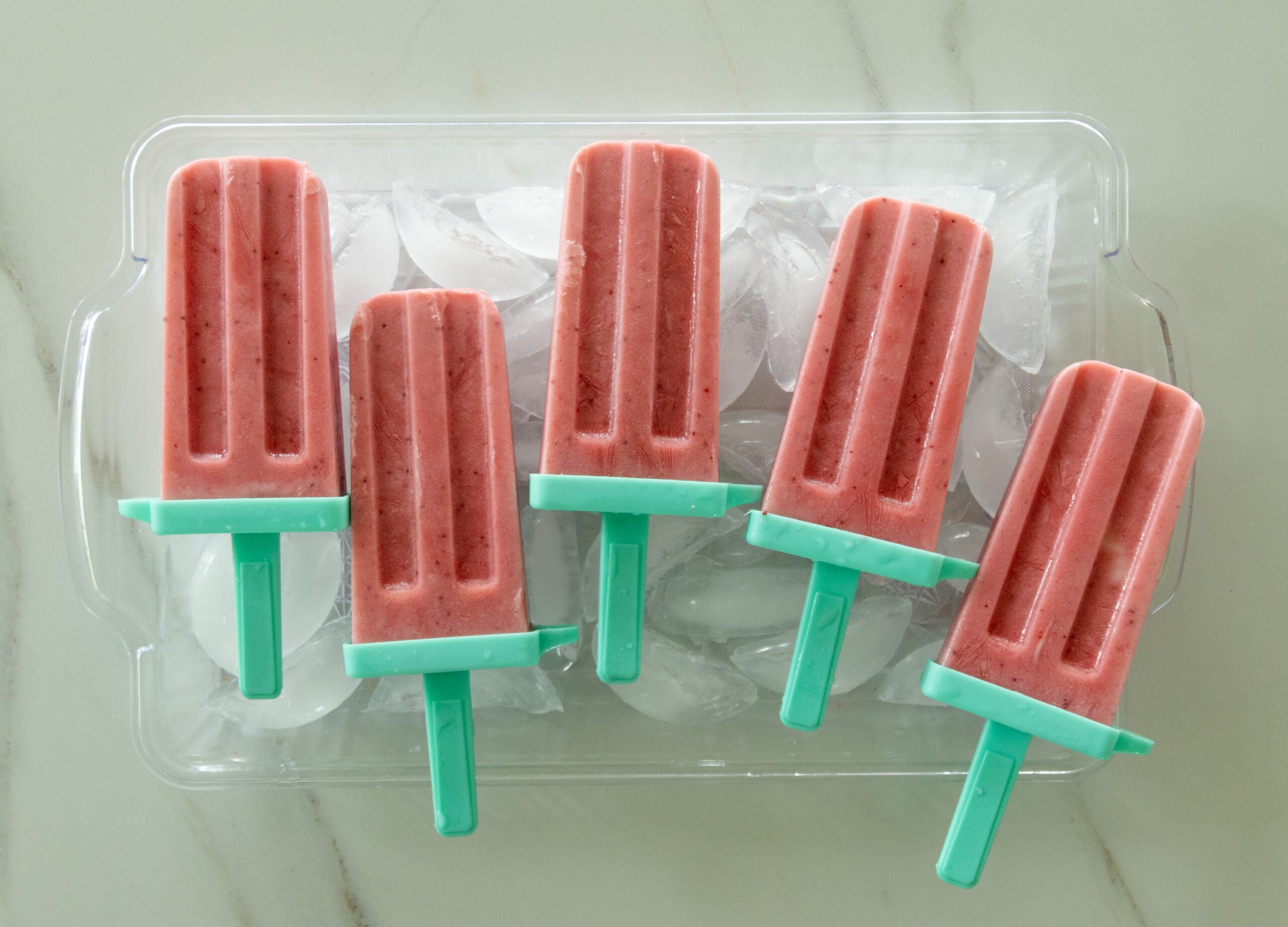 strawberry yogurt popsicles on a tray of ice cubes