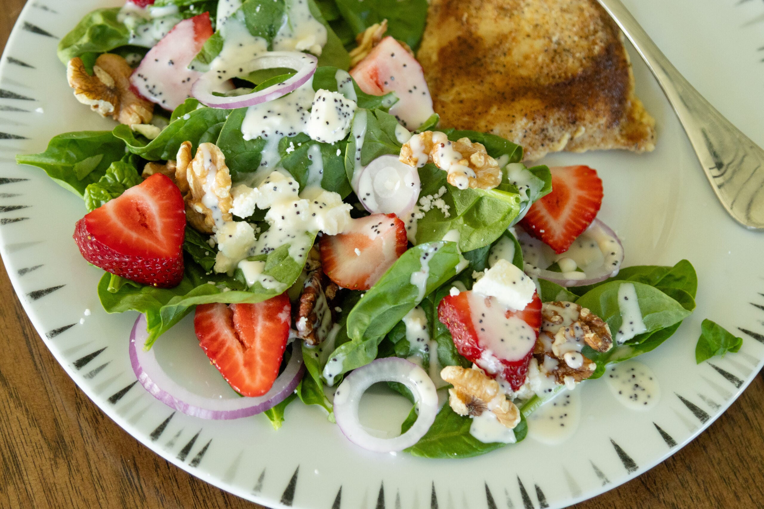a serving of strawberry spinach feta salad on a plate with a piece of chicken