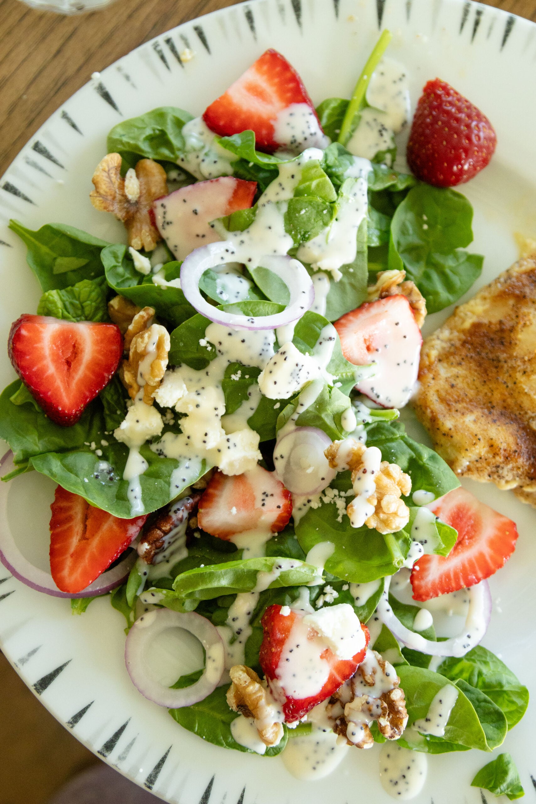 a serving of strawberry spinach feta salad on a plate with a piece of chicken