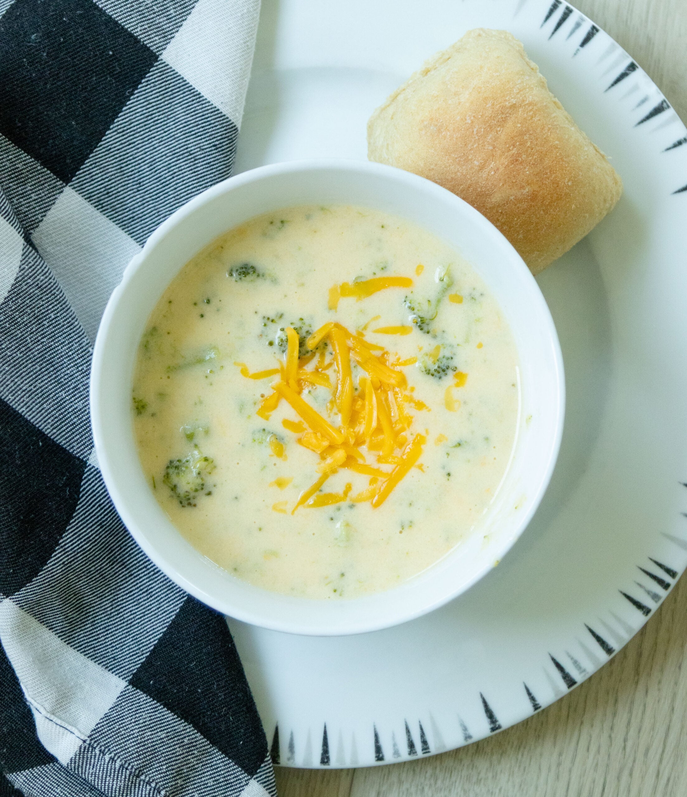a bowl of broccoli cheddar soup on a plate with a dinner roll 