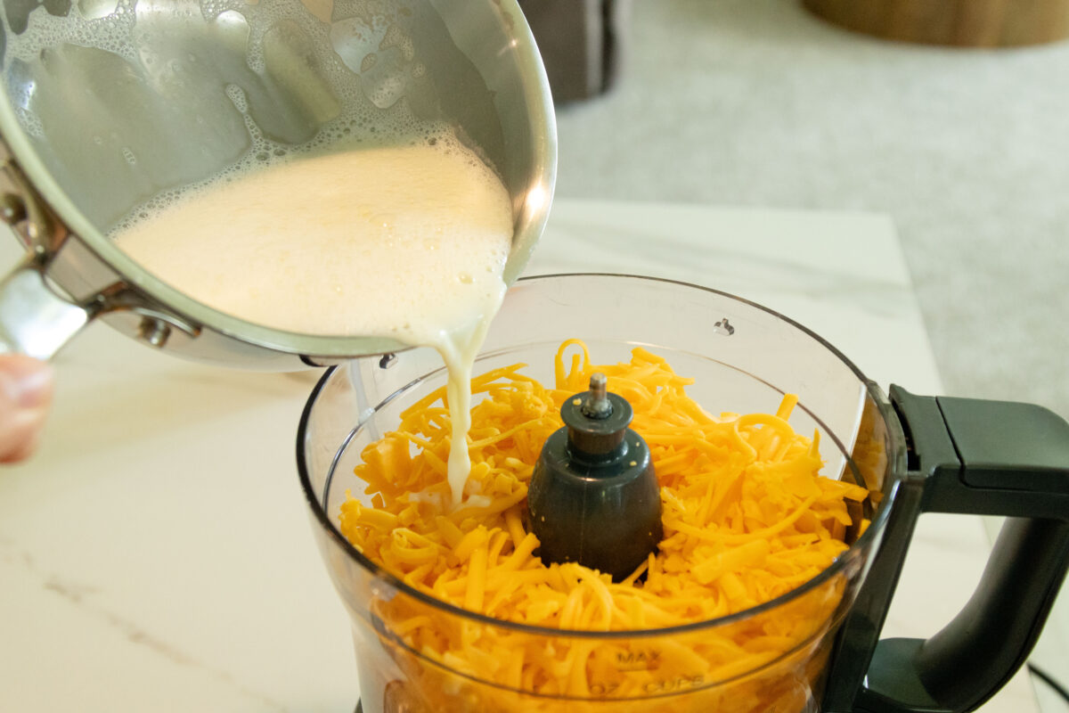 pouring the milk in on top of the cheese in the food processor