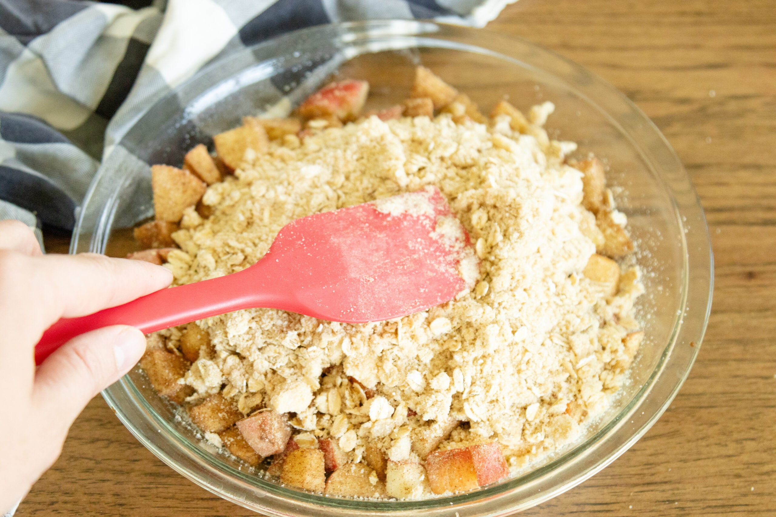 spatula spreading the crumble mixture on top of the apple chunks